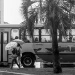 Pessoa caminhando com guarda-chuva em uma rua chuvosa; imagem ilustrativa para orientações de segurança em dia de chuva.
