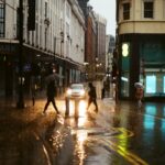 Pedestres caminham sob chuva em uma rua urbana; imagem ilustrativa, não retrata necessariamente Duque de Caxias.